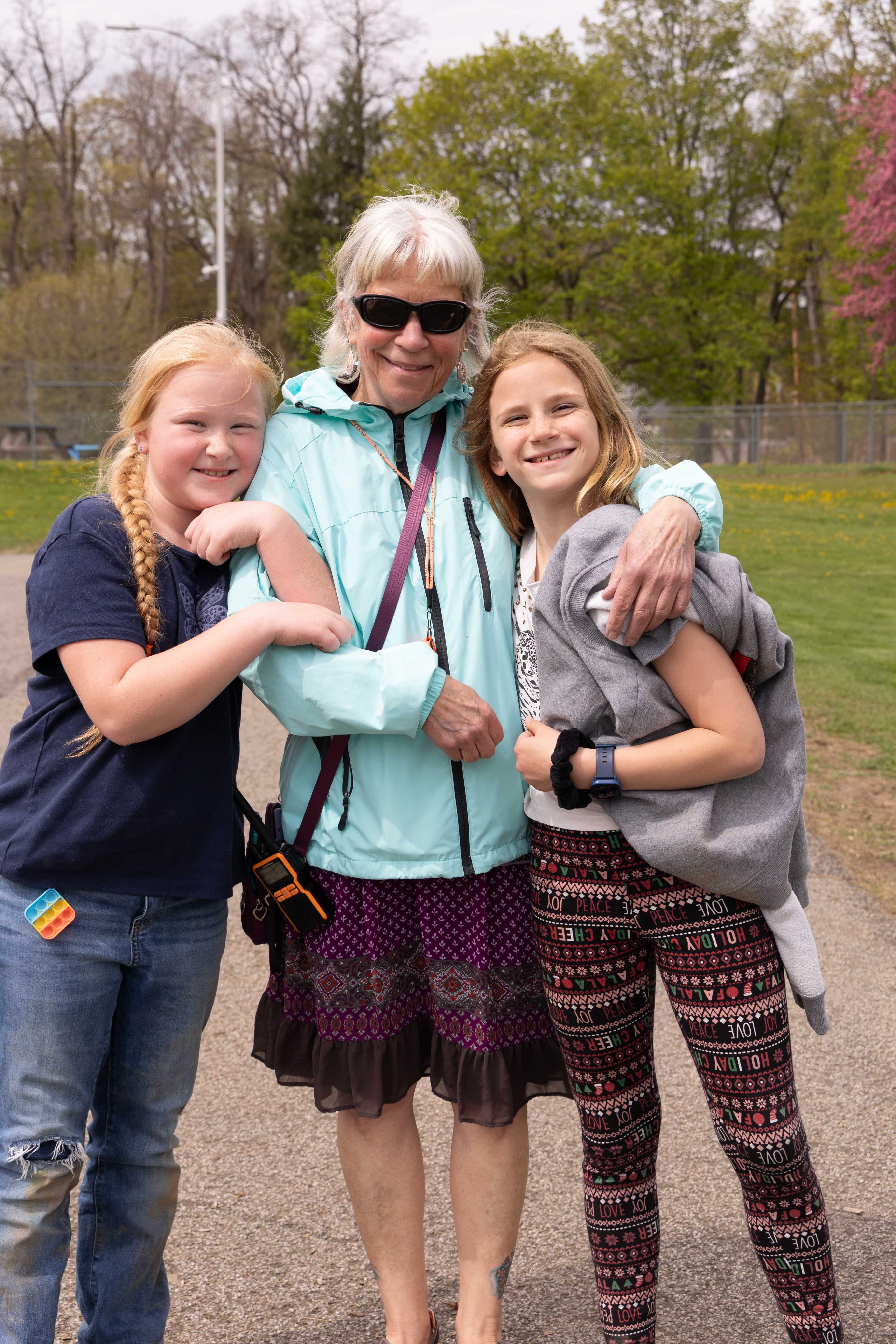 Two young girls pose with Ms. Patty at recess on the playground